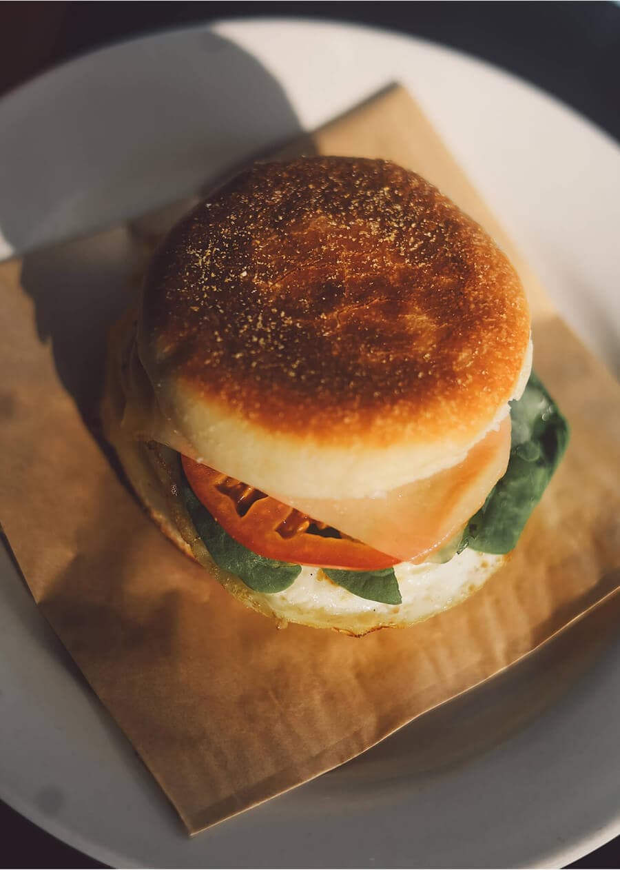 Breakfast sandwich with ham, tomato, and spinach on a toasted English muffin.
