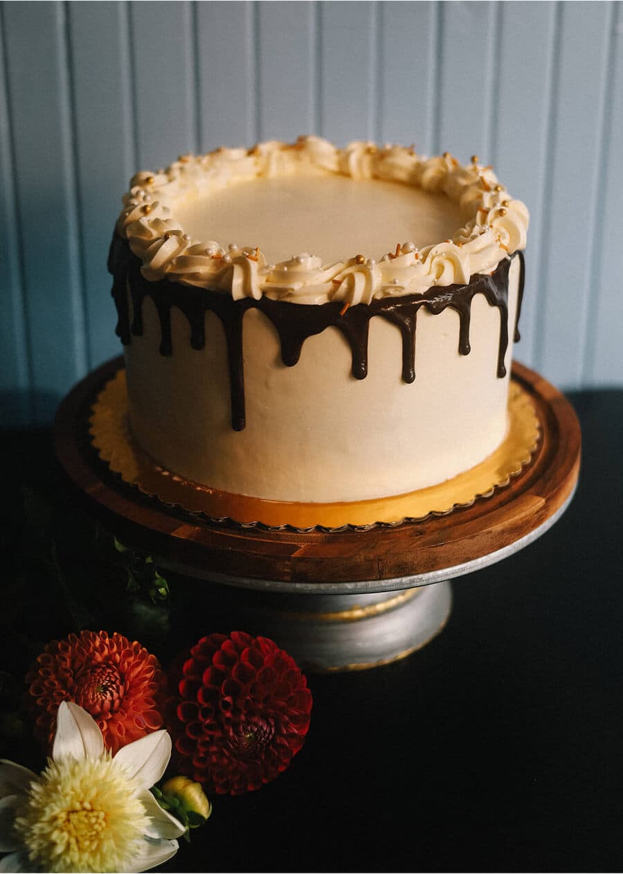 Double chocolate layer cake with ganache drips and piped rosettes on a wooden stand.