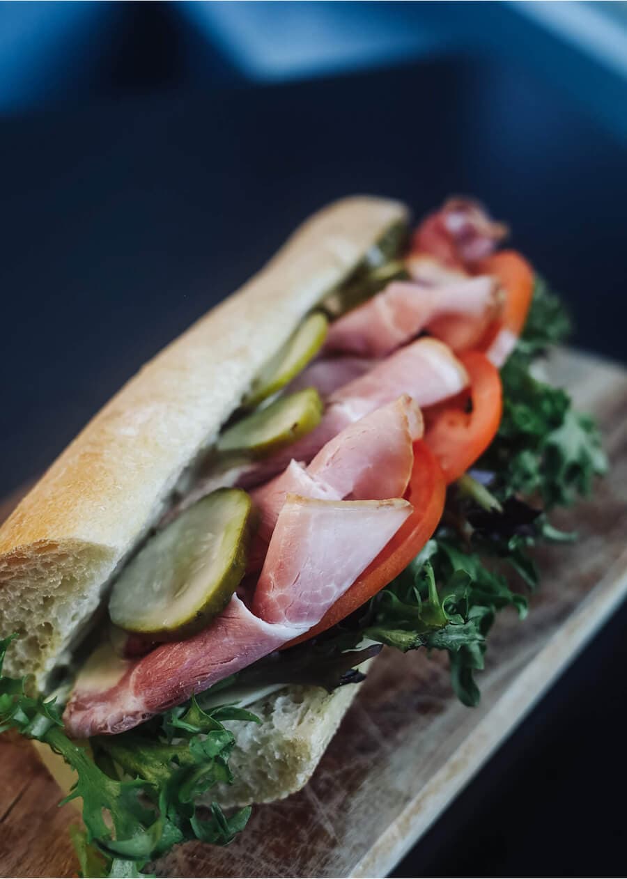 Ham and cheese baguette sandwich with lettuce, tomato, and pickles.