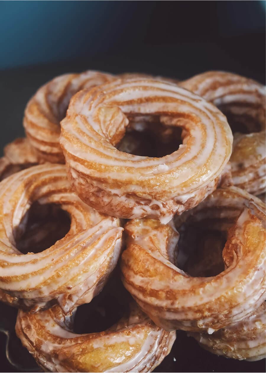 Pile of glazed vanilla crullers showing a golden, airy, twisted texture.